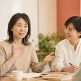 緊張しながらも英会話レッスンで話し始める大人女性と見守る講師・受講生