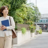 藤沢の緑ある街並みを英語のノートを持って歩く大人女性