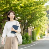 鎌倉の緑ある街並みをノートを持って歩く大人女性