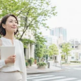 東京都港区の緑ある街並みをノートを持って歩く大人女性