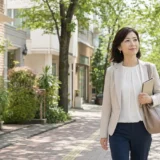 桜新町の緑ある住宅街をノートを持って歩く大人女性